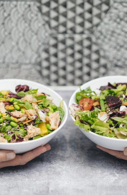 Two pairs of hands holding salads in bowls