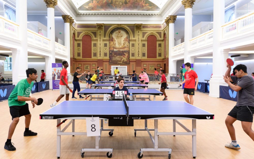 Young people playing table tennis in a large hall