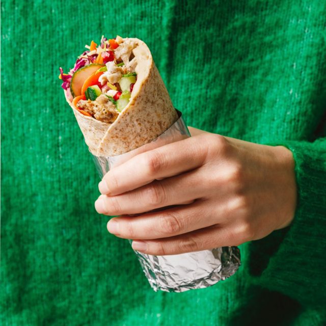 A photo of a delicious wrap with bright ingredient fillings held in a hand