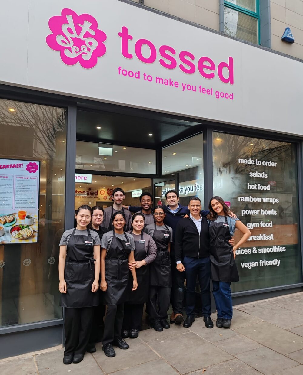 A group of ten people, some in uniforms and aprons, stand smiling outside a \